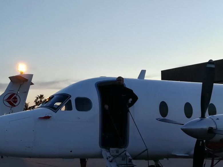 The nose of a white Beechcraft 1900D at dusk, airstair open.