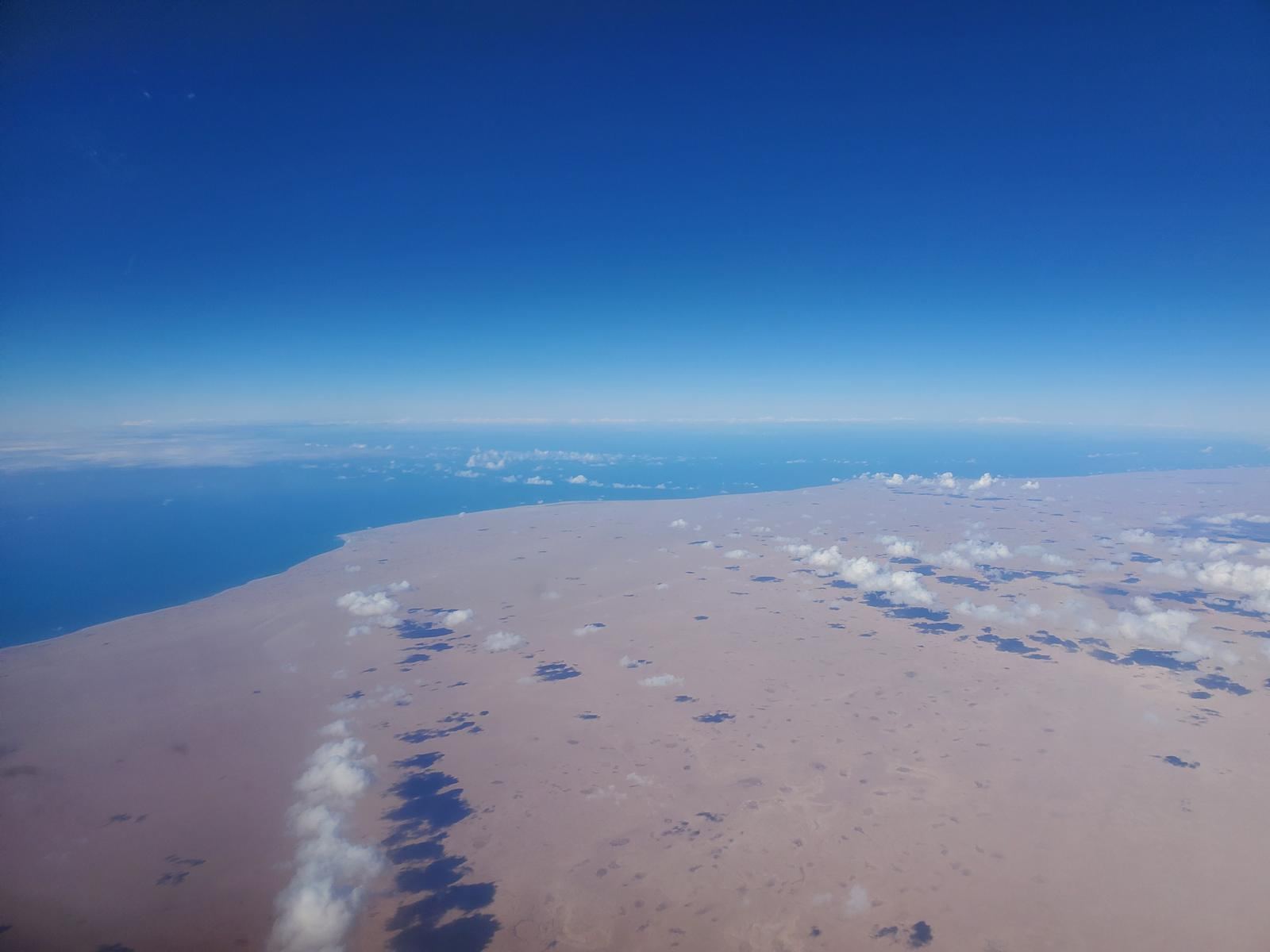 A desert coastline seen from altitude, with cloud shadows.