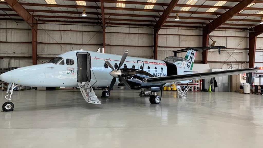 A pale blue Beechcraft 1900D air ambulance with MEDI titles and a star of life, in a hangar with its airstair down.