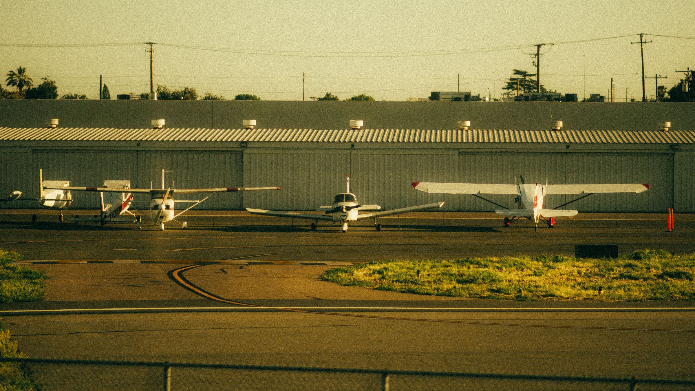 Several light aircraft parked in a row in front of a hangar at golden hour.