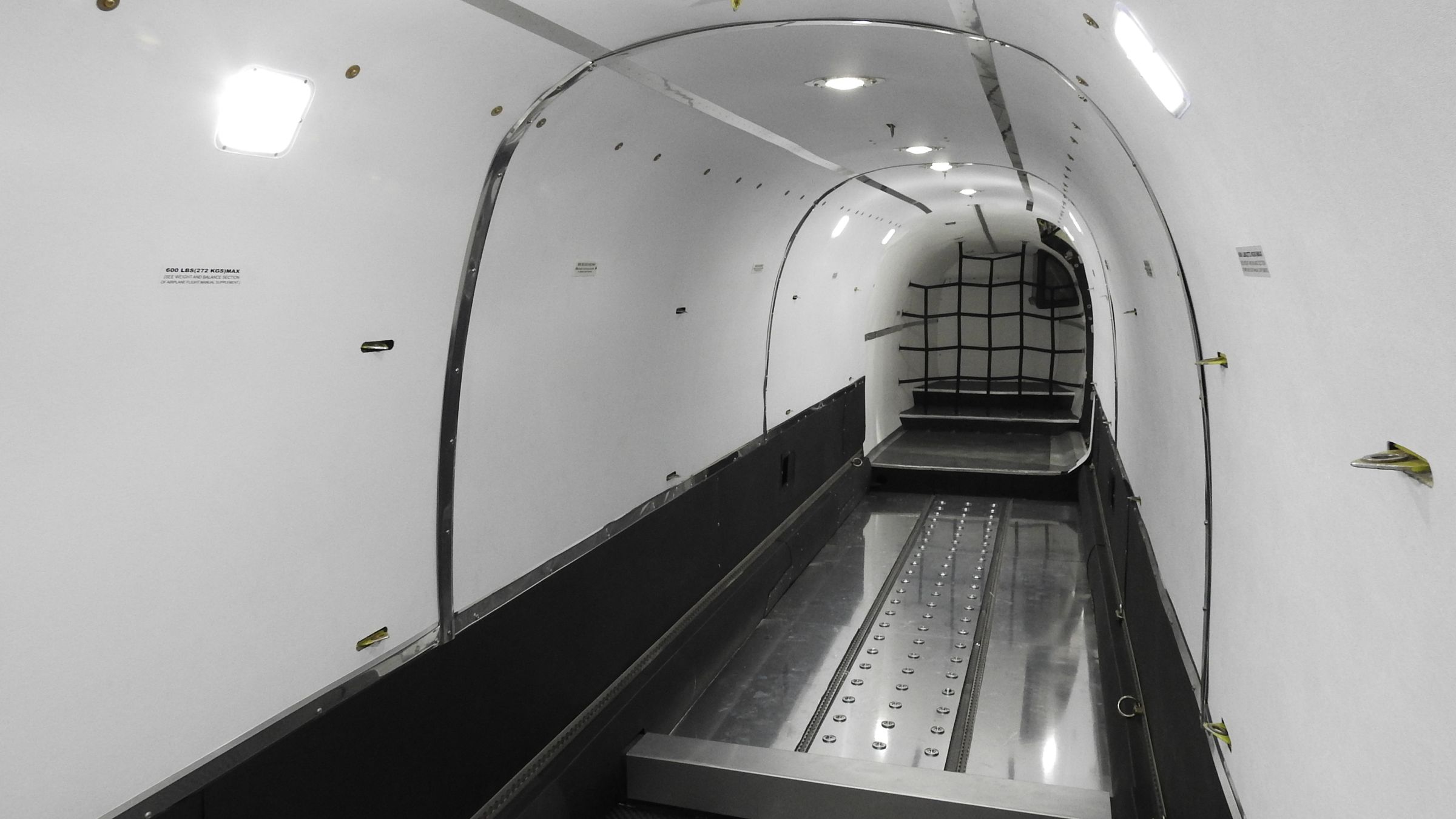 An empty white cargo cabin with a roller ball floor, tie-down rails and a restraint net at the far end.
