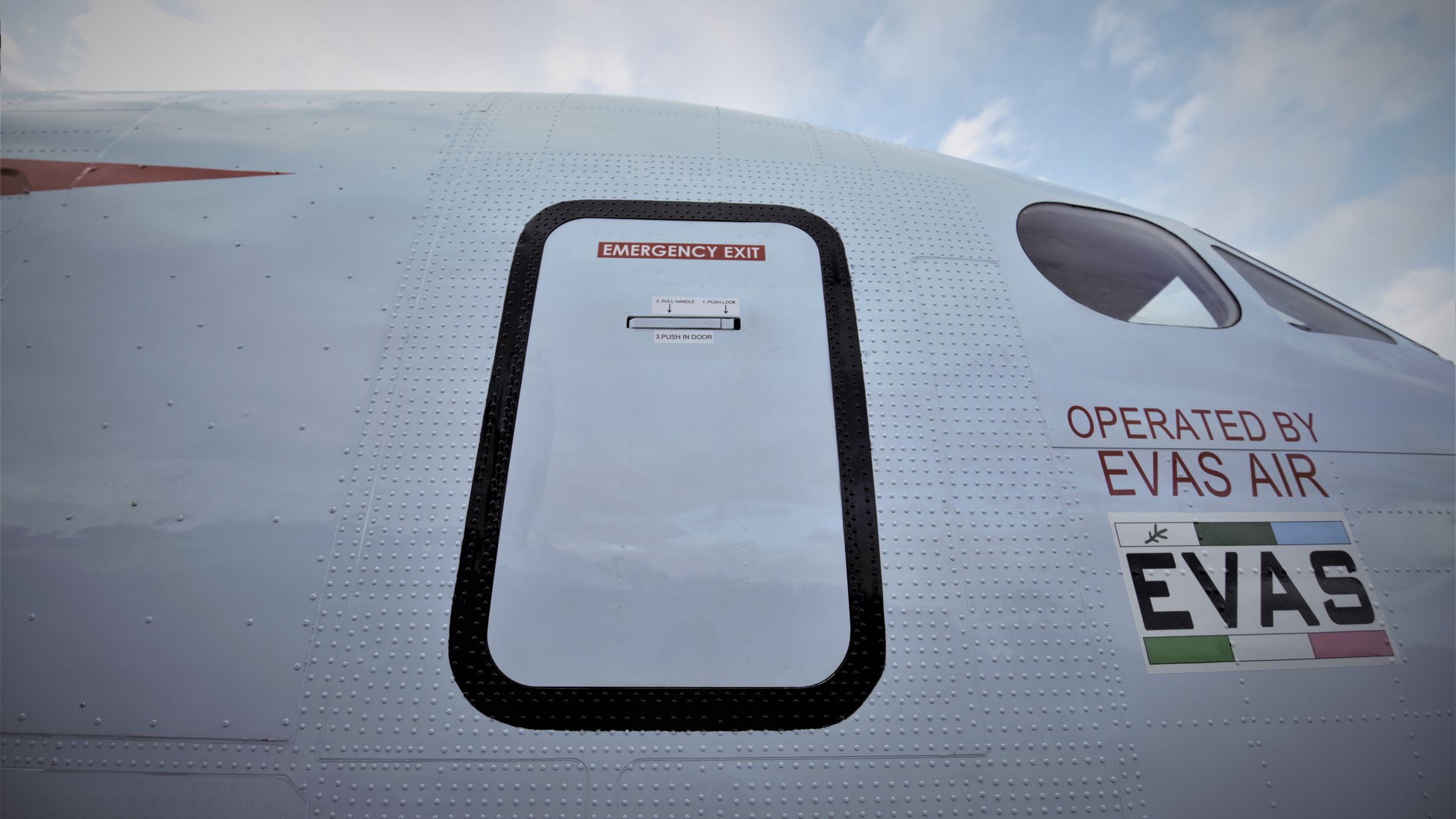 The emergency exit and Operated by EVAS Air marking on the fuselage of a Beechcraft 1900D.